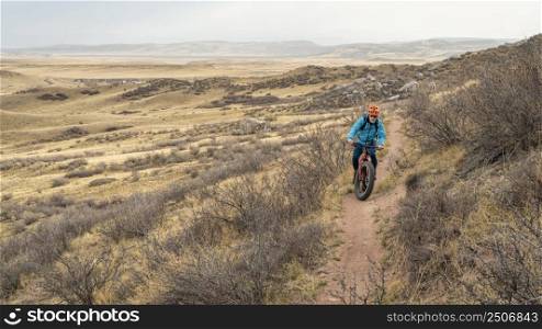 lonely cyclist riding fat mountain bike on a single track trail in northern Colorado grassland, early spring scenery in Soapstone Prairie Natural Area near Fort Collins