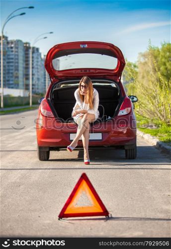 Lonely depressed woman sitting on trunk of broken car