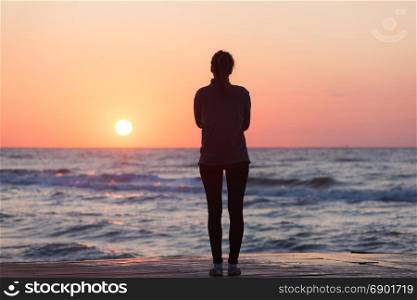 Lonely girl standing on the sunrise beach. Woman silhouette over sunrise sky