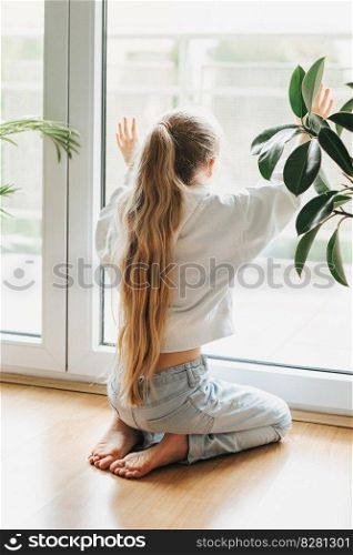 Lonely sad little girl sitting by the window.