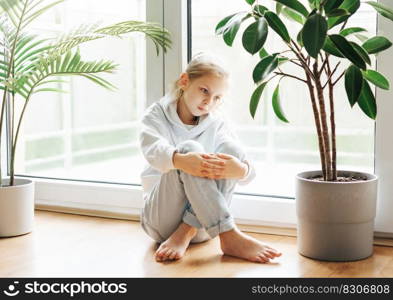 Lonely sad little girl sitting by the window.