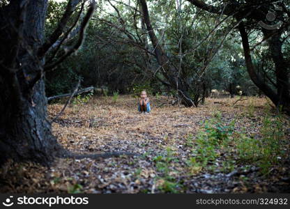 Lonely sad little girl squatting in the forest. Feelings concept.