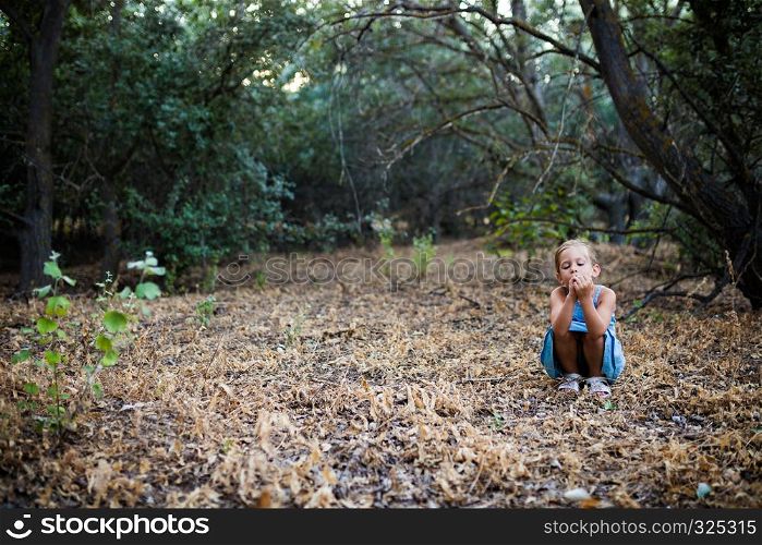 Lonely sad little girl squatting in the forest. Feelings concept.