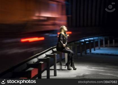 Lonely sad woman sitting at night at highway with cars rushing past her