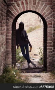 Lonely Teenager Girl Standing in the Brick Ruins and Drinking Beer in a Sweatshirt with a Hood