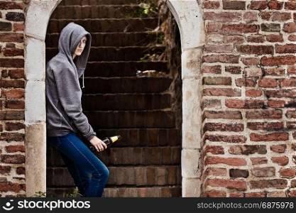 Lonely Teenager Girl Standing in the Brick Ruins and Drinking Beer in a Sweatshirt with a Hood