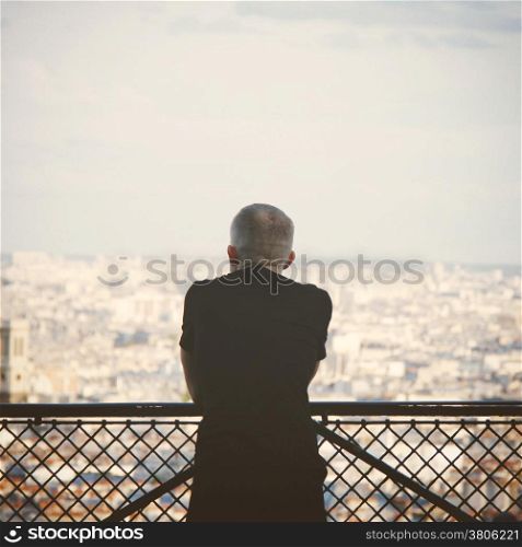 Lonely tourist man overlooks view Paris skyline, retro filter effect