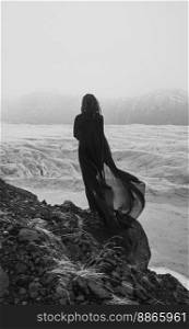 Lonely woman with fabric cape on rock monochrome scenic photography. Picture of person with ancient iceberg on background. High quality wallpaper. Photo concept for ads, travel blog, magazine, article. Lonely woman with fabric cape on rock monochrome scenic photography