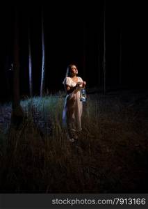 Lonely woman with gas lamp standing in scary dark forest