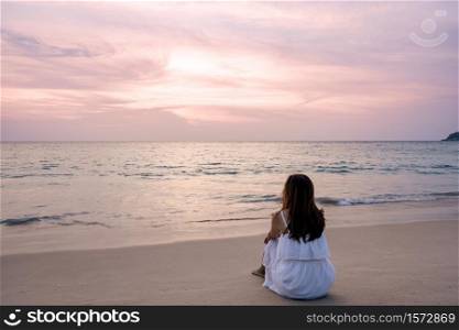 Lonely young asian woman sitting on the beach at sunset