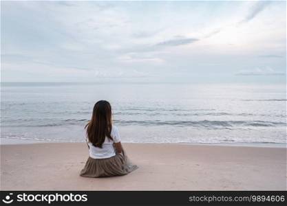 Lonely young asian woman sitting on the beach at sunset