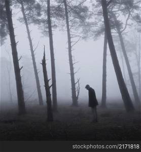 lonesome figure of man with cap between trunks of pine trees in misty forest