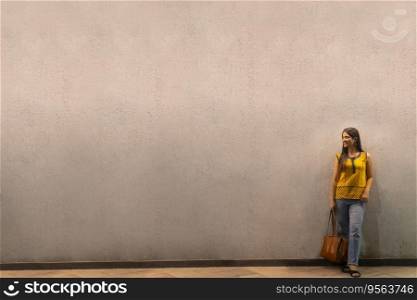 Long distance shot of an Indian woman with bag standing against wall