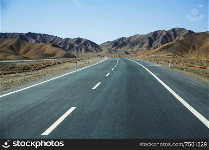 Long empty asphalt road in desert with clear blue sky .