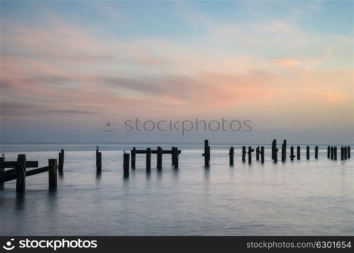 Long exposure landscape image of colorful sunrise over ocean and derelict pier in distance