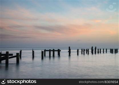 Long exposure landscape image of colorful sunrise over ocean and derelict pier in distance