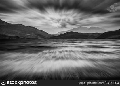 Long exposure landscape of mountains and stormy sky over lake in black and white