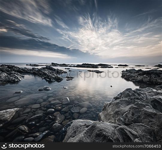 Long exposure landscape with the rocky coast of Black sea at the end of the day. Cloundscape over the calm water and grey dramatic rocks.