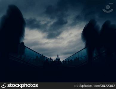 Long exposure of pedestrians at London, England, UK Millenium Bridge with St. Paul&rsquo;s Cathedral in background - dystopia dark post-apocalyptic fine art concept. Long exposure of pedestrians at London, England, UK Millenium Bridge with St. Paul&rsquo;s Cathedral in background - dystopia dark post-apocalyptic fine art concept.