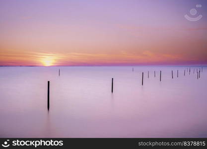 Long exposure picture of a fyke at the IJsselmeer with the endless horizon during an atmospheric sunset in spring. Beautiful lake with a fyke at sunset.