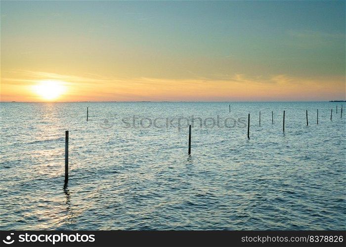 Long exposure picture of a fyke at the IJsselmeer with the endless horizon during an atmospheric sunset in spring. Beautiful lake with a fyke at sunset.