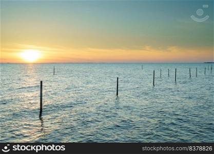 Long exposure picture of a fyke at the IJsselmeer with the endless horizon during an atmospheric sunset in spring. Beautiful lake with a fyke at sunset.
