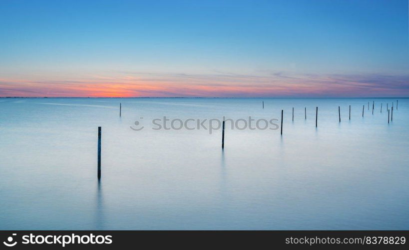 Long exposure picture of a fyke at the IJsselmeer with the endless horizon during an atmospheric sunset in spring. Beautiful lake with a fyke at sunset.