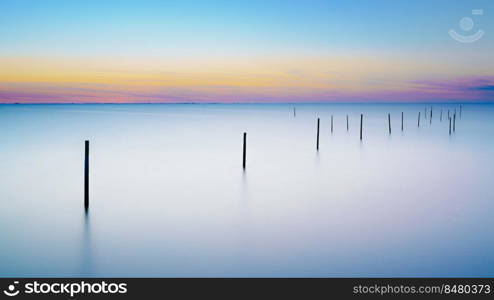 Long exposure picture of a fyke at the IJsselmeer with the endless horizon during an atmospheric sunset in spring. Beautiful lake with a fyke at sunset.