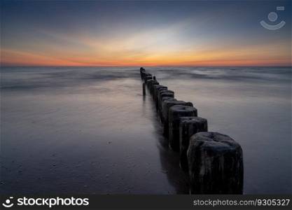 long exposure view of an ocean sunset with sandy beach and wooden pylon storm groin in the foreground