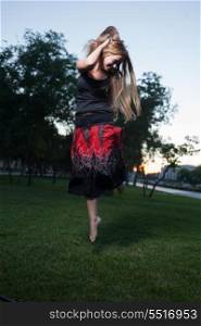 Long haired and free. Young women make jump outdoors at evening. Vertical shot.