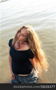 Long haired blonde posing in lake backlit by sun.