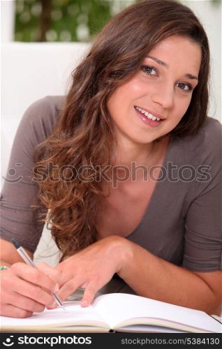 Long haired girl writing in a hardback notebook