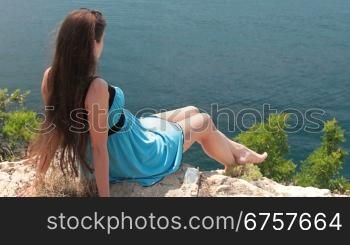 long-haired young woman resting on top of a mountain near the sea