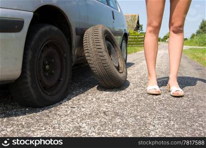 Long legged woman standing next to her car with a flat tire, the spare waiting to be put on