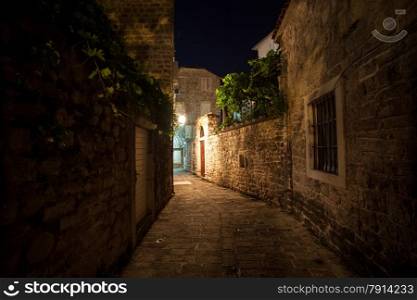 Long old narrow street lit by gas lanterns at night