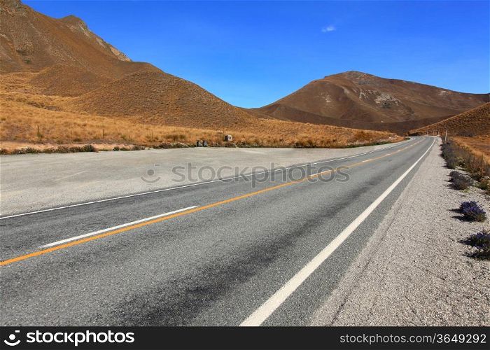 Long road stretching out to dry mountain range at Lindis Pass, the highest highway, in NewZealand
