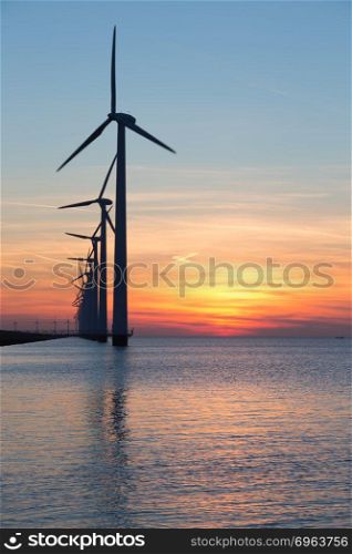 Long row of windturbines with sunset over the sea