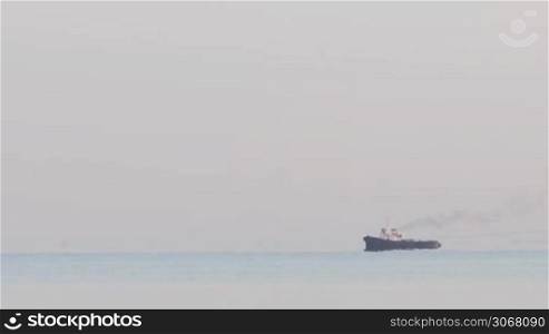 Long shot of tugboat tugging a large barge in an overcast day and calm sea