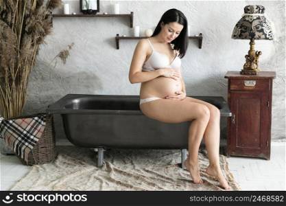 long shot pregnant woman sitting bathtub
