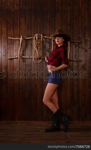 long-standing girl dressed as a cowboy wearing a traditional wide-brimmed hat and shertah posing against a wooden background and a ladder