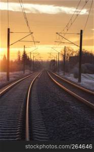 Long straight railway tracks passing through German village and frozen nature, at the golden hour. Holiday travel concept. Industrial landscape.