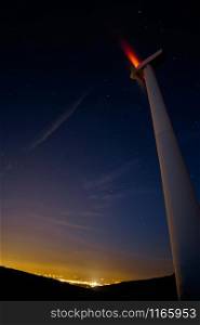 Long time exposure of wind turbine at night with an almost clear sky and the city lights. Wind turbine at night with city lights