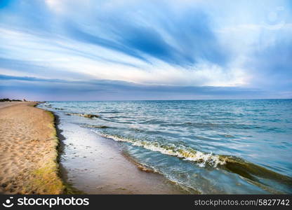 Long tropical beach with yellow sand and blue sea with waves, white clouds on background