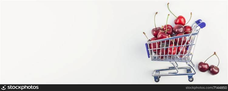 Long wide banner of ripe cherries in a shopping cart with copy space isolated on white background in minimal style. Concept of supermarket or fruit market shopping. Template for your text or design.