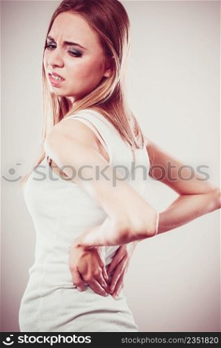 Long working hours and health. Young female with backache. Woman with back pain on gray