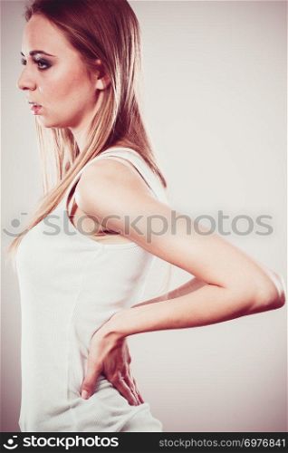 Long working hours and health. Young female with backache. Woman with back pain on gray