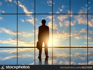 Long working hours. Silhouette of businessman against panoramic office window