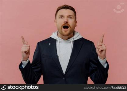 Look, its awesome. Portrait of excited young ginger guy in fashionable casual clothes raising index fingers and pointing up with amazed face expression. Promotion and discount concept. Shocked ginger man pointing up with index fingers with wow face expression