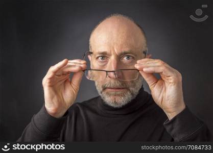 look over reading glasses - headshot of 60 years old man with a beard against a black background