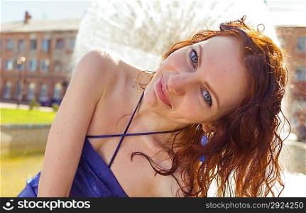 looking at camera redhead women near fountain in summertime. Shot full of sunshine, Sunlit